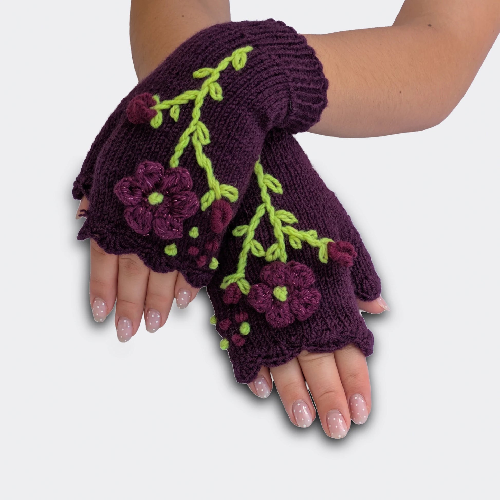 Mitaines violettes portées mains croisées, tricotées main avec fleurs appliquées, paillettes légères et tiges vert clair.