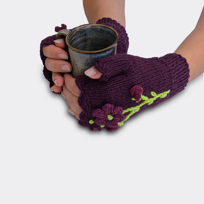 Mitaines violettes tenant une tasse, avec fleurs appliquées, légères paillettes et bord supérieur festonné au crochet.