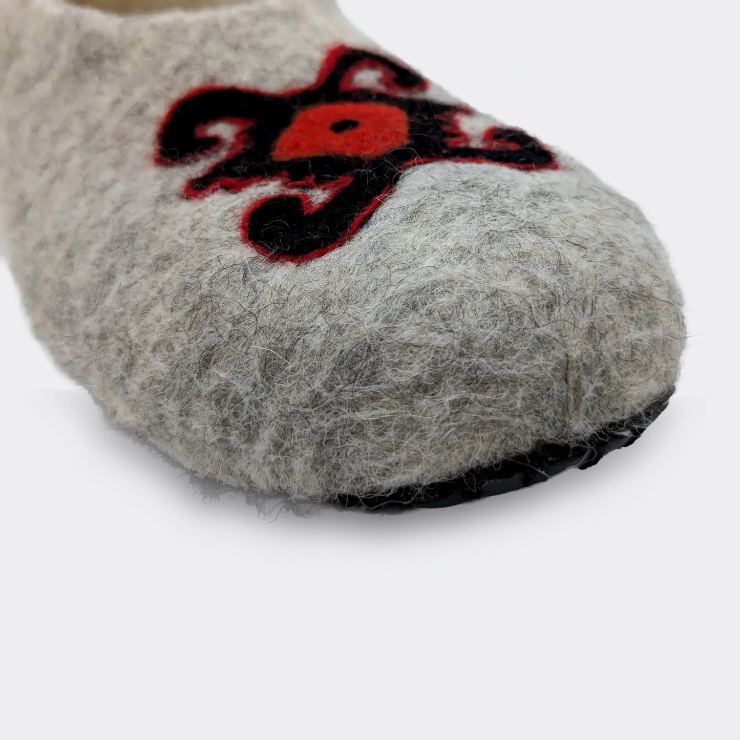 Détail du dessin de tortue sur chausson en feutre gris. Le motif ancien symbolise stabilité et mémoire dans l’art textile de Pirot. Vue en gros plan.