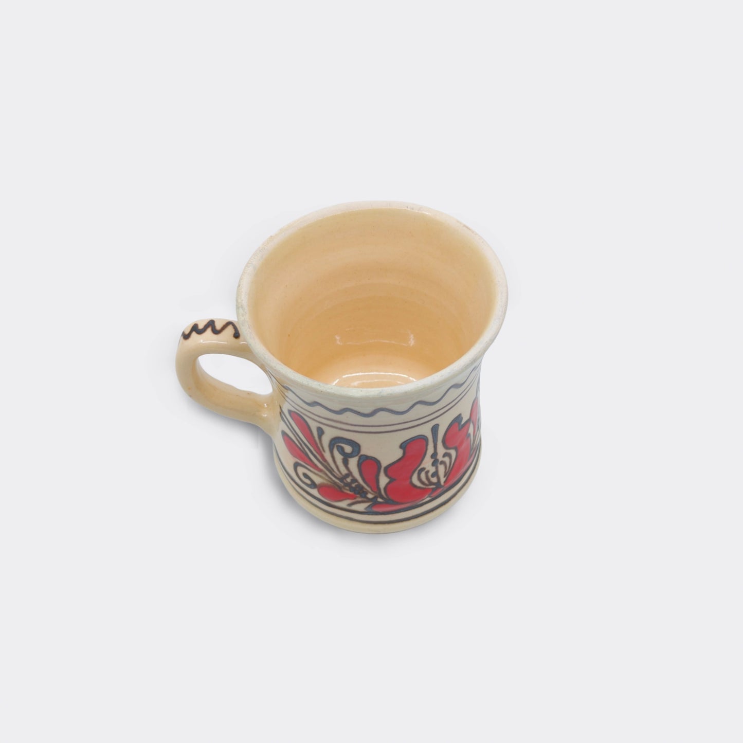 Mug en céramique de Corund vu du dessus, intérieur émaillé crème et bord brut. Tasse artisanale roumaine faite main. Décor floral rouge extérieur.