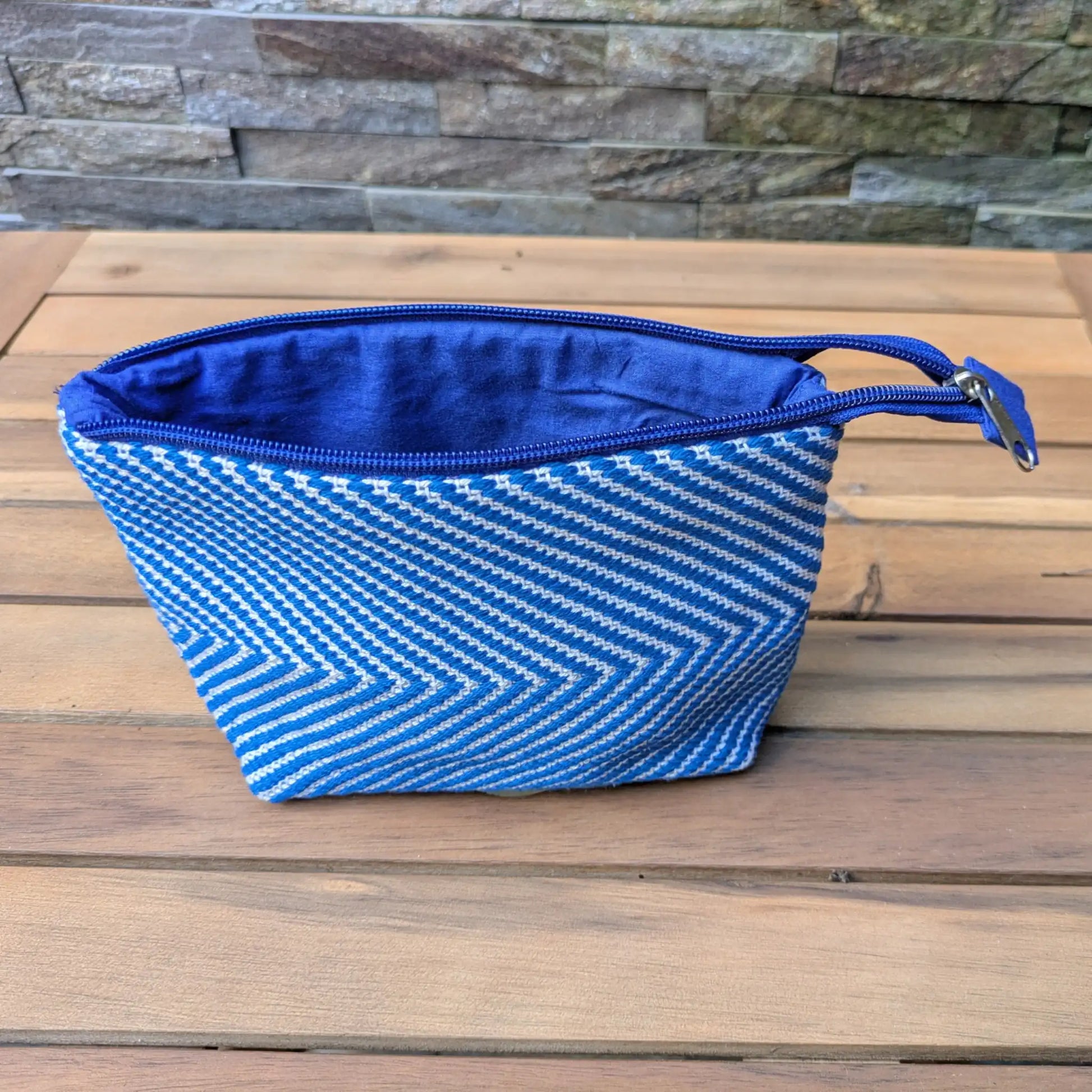 Nécessaire de toilette tissé main en chevrons bleu et blanc, ouvert sur une doublure textile bleue.