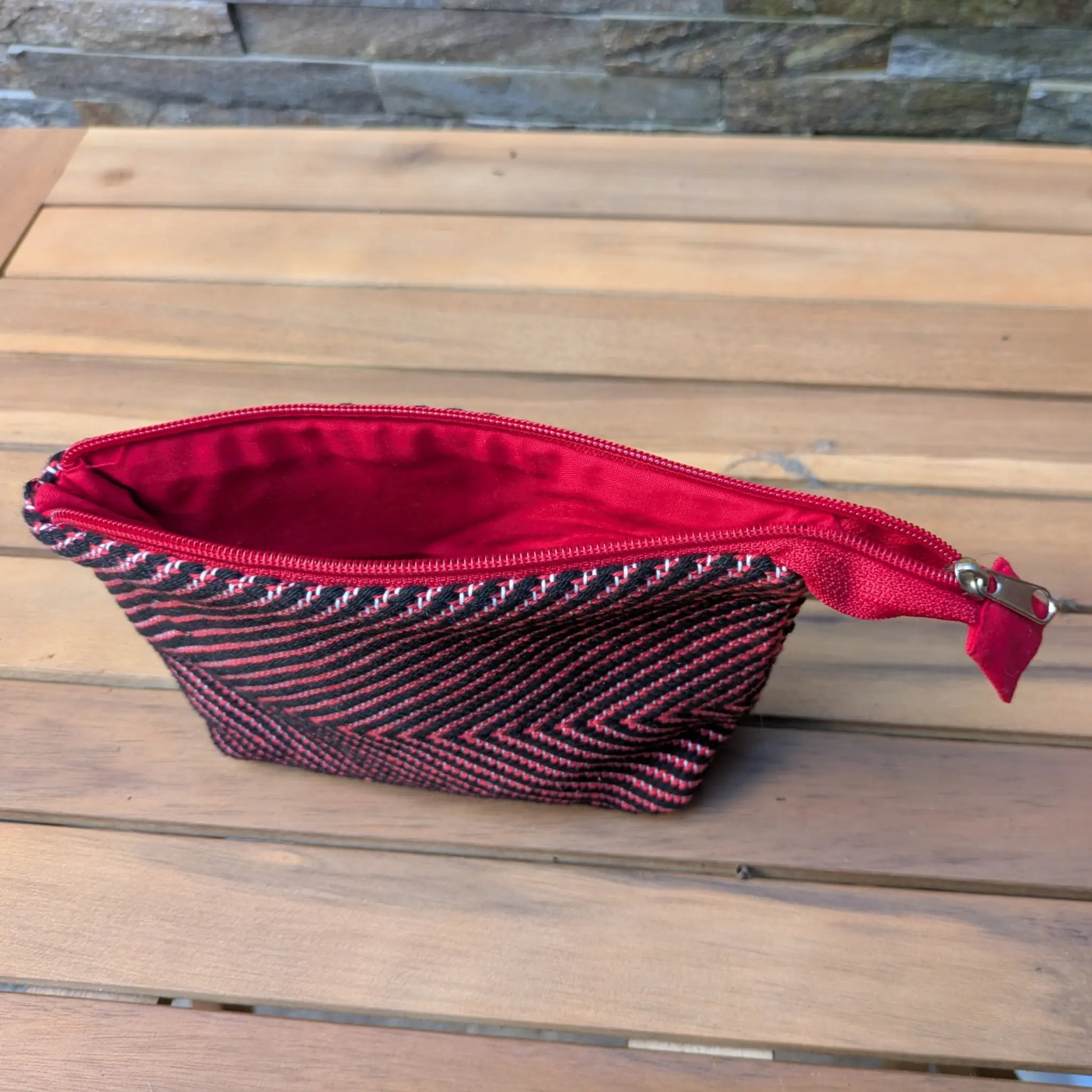Nécessaire de toilette tissé main en chevrons rouge et noir, ouvert sur une doublure textile rouge.