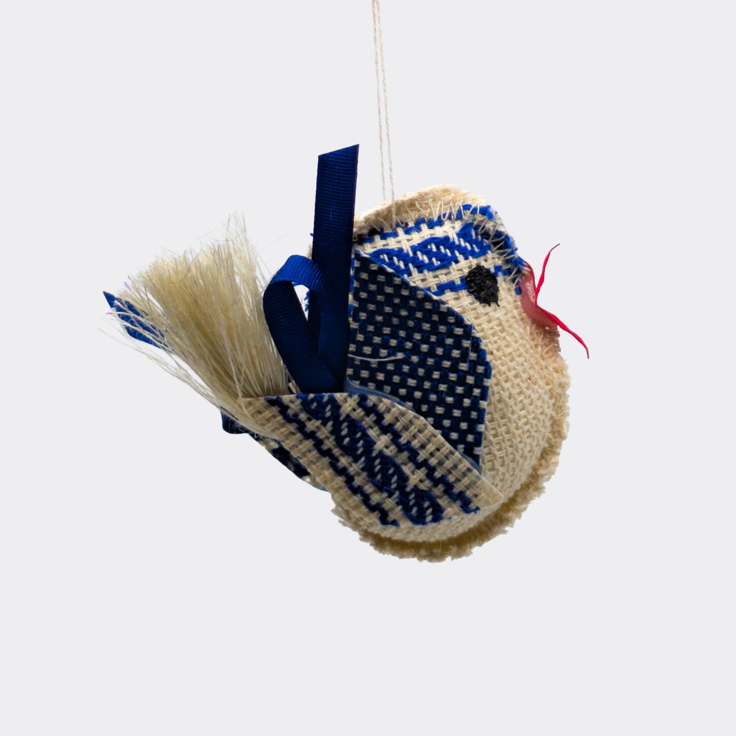 Petit oiseau bleu en tissu avec frise tissée sur la tête. Le corps écru est rembourré et les ailes sont faites de motifs bleus. Une décoration à suspendre légère et artisanale.