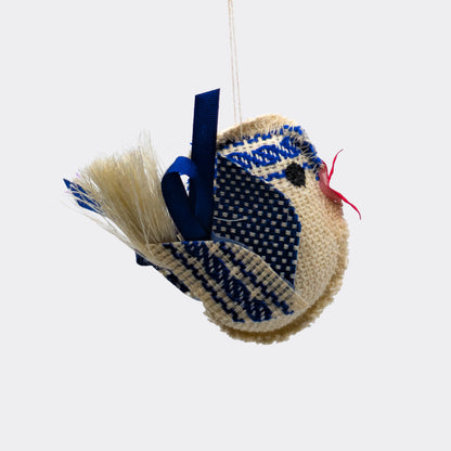 Petit oiseau bleu en tissu avec frise tissée sur la tête. Le corps écru est rembourré et les ailes sont faites de motifs bleus. Une décoration à suspendre légère et artisanale.