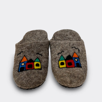 Pantoufles artisanales en laine grise ornées de petites maisons stylisées et joyeusement colorées, vue de face.