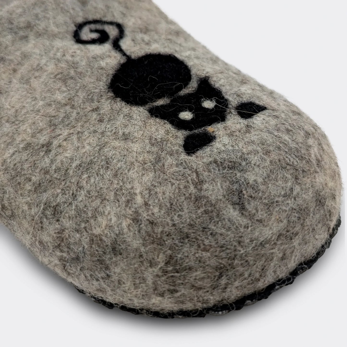 Gros plan sur le dessin de chat noir sur une pantoufle en feutre gris, laine naturelle de Serbie. Réalisé sur place. Vue de détail.