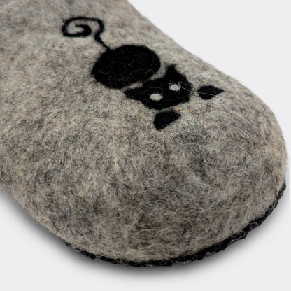 Gros plan sur le dessin de chat noir sur une pantoufle en feutre gris, laine naturelle de Serbie. Réalisé sur place. Vue de détail.