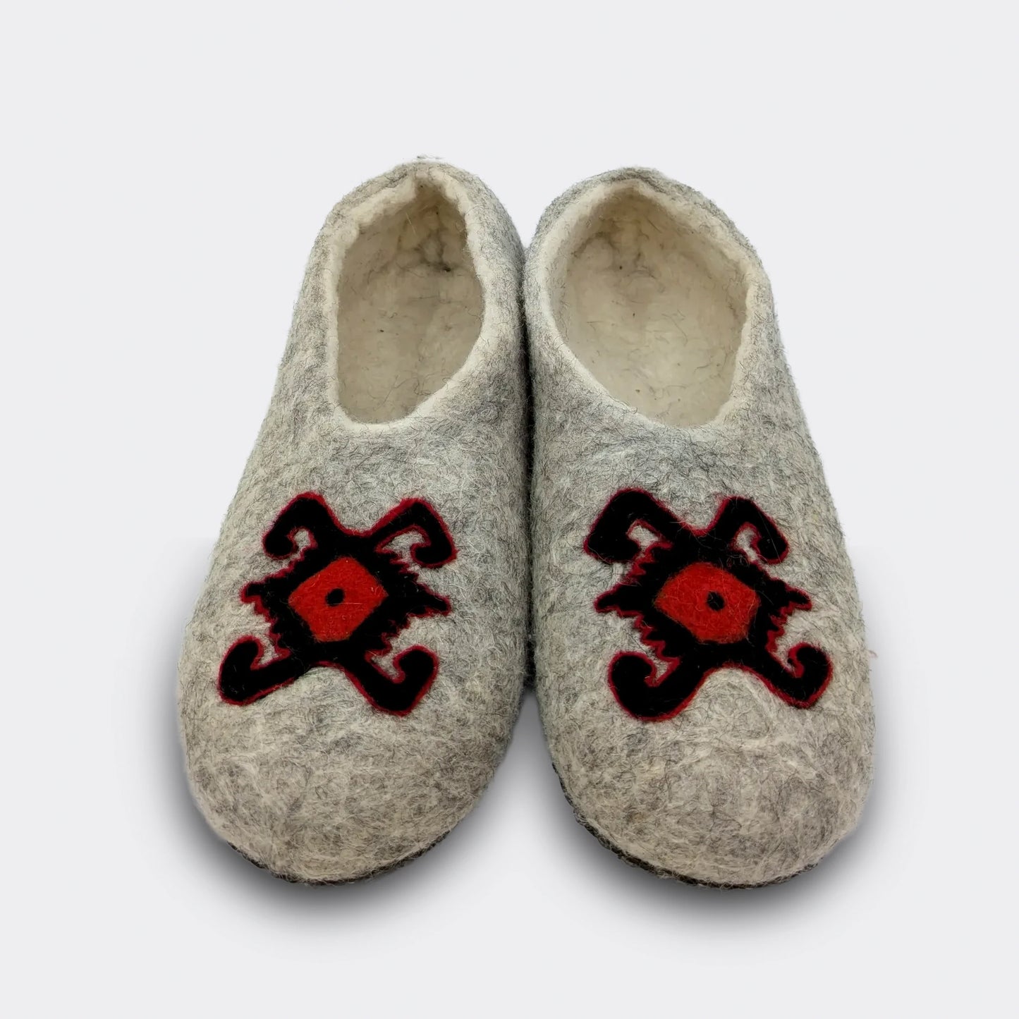 hausson en feutre gris vu de face, décoré du motif de la tortue des kilims de Pirot. Le dessin rouge et noir symbolise longévité et protection. La laine naturelle garde la mémoire d’un artisanat ancien. Vue de face.