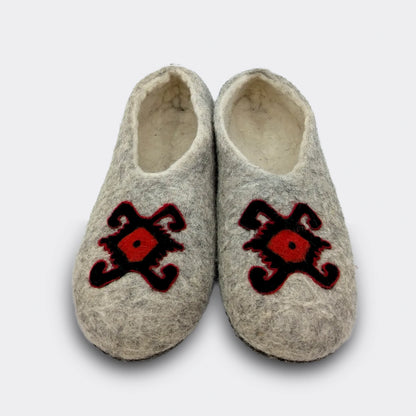 hausson en feutre gris vu de face, décoré du motif de la tortue des kilims de Pirot. Le dessin rouge et noir symbolise longévité et protection. La laine naturelle garde la mémoire d’un artisanat ancien. Vue de face.