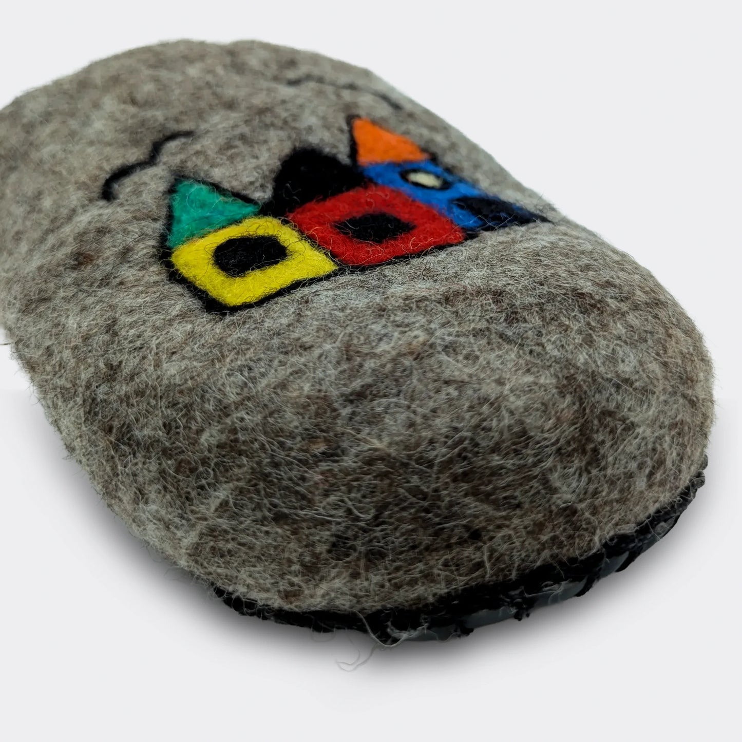 Zoom sur le dessin naïf de maisons appliqué sur une pantoufle en feutre artisanal gris, style folklorique, vue en gros plan.
