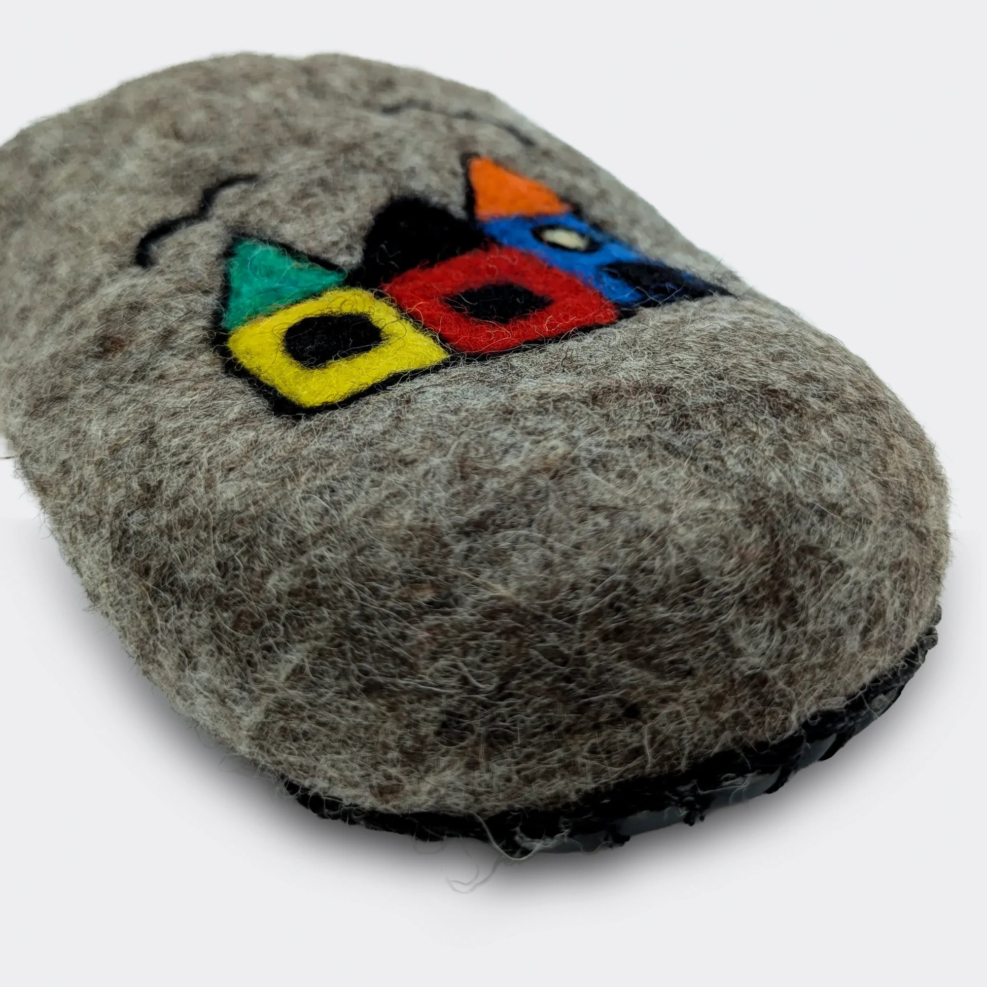 Zoom sur le dessin naïf de maisons appliqué sur une pantoufle en feutre artisanal gris, style folklorique, vue en gros plan.