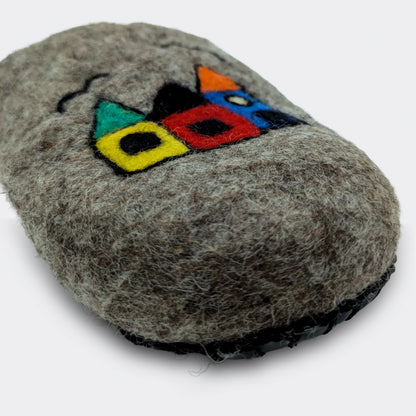 Zoom sur le dessin naïf de maisons appliqué sur une pantoufle en feutre artisanal gris, style folklorique, vue en gros plan.