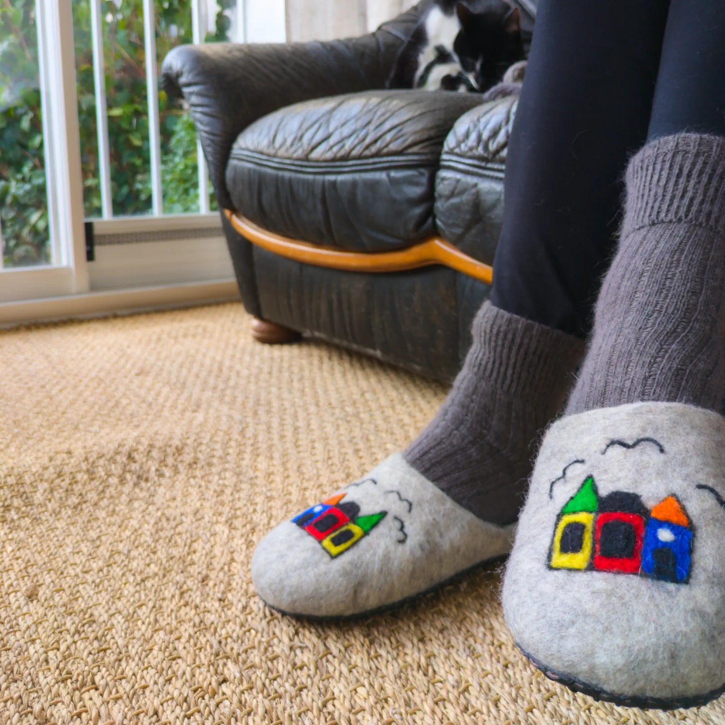 Une femme perte des pantoufles avec des maisons colorés dessinées dessus. Les pantoufles sont en feutre et réalisées à la main