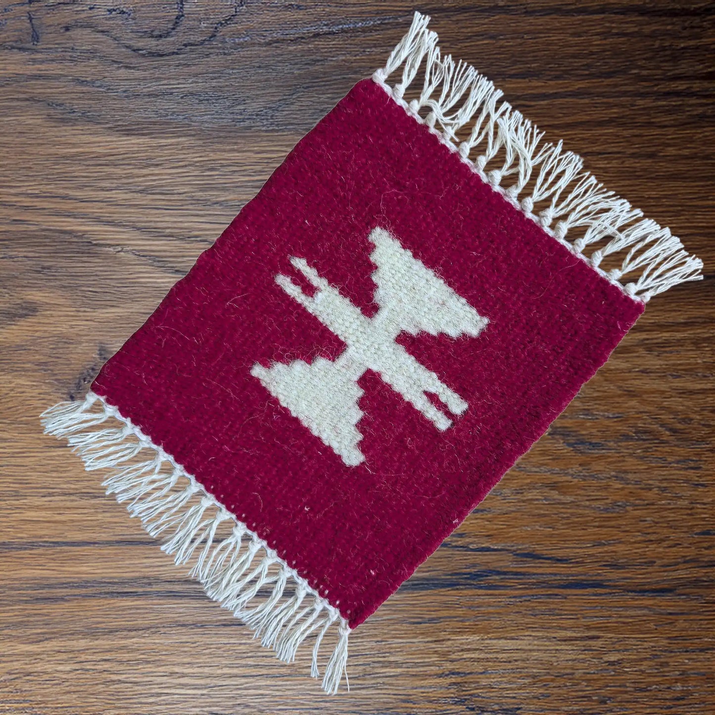 Mini tapis en laine rouge et motif blanc, posé sur une surface bois. Un petit textile artisanal discret aux accents balkaniques.