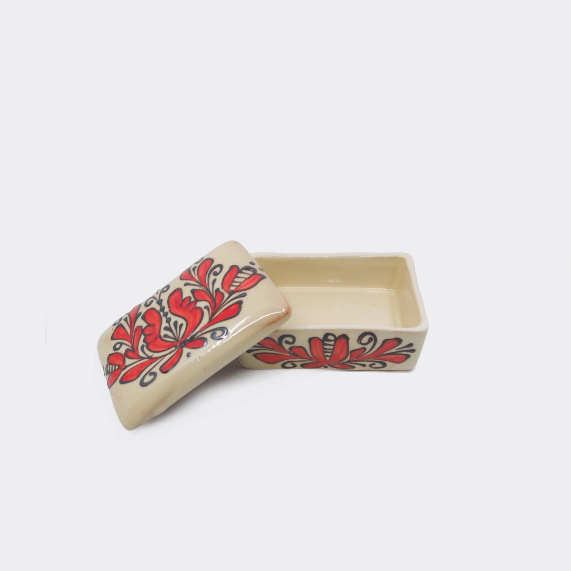 Boîte en céramique artisanale de Corund décorée de fleurs rouges stylisées. Le fond crème émaillé contraste avec les motifs floraux peints à la main.
