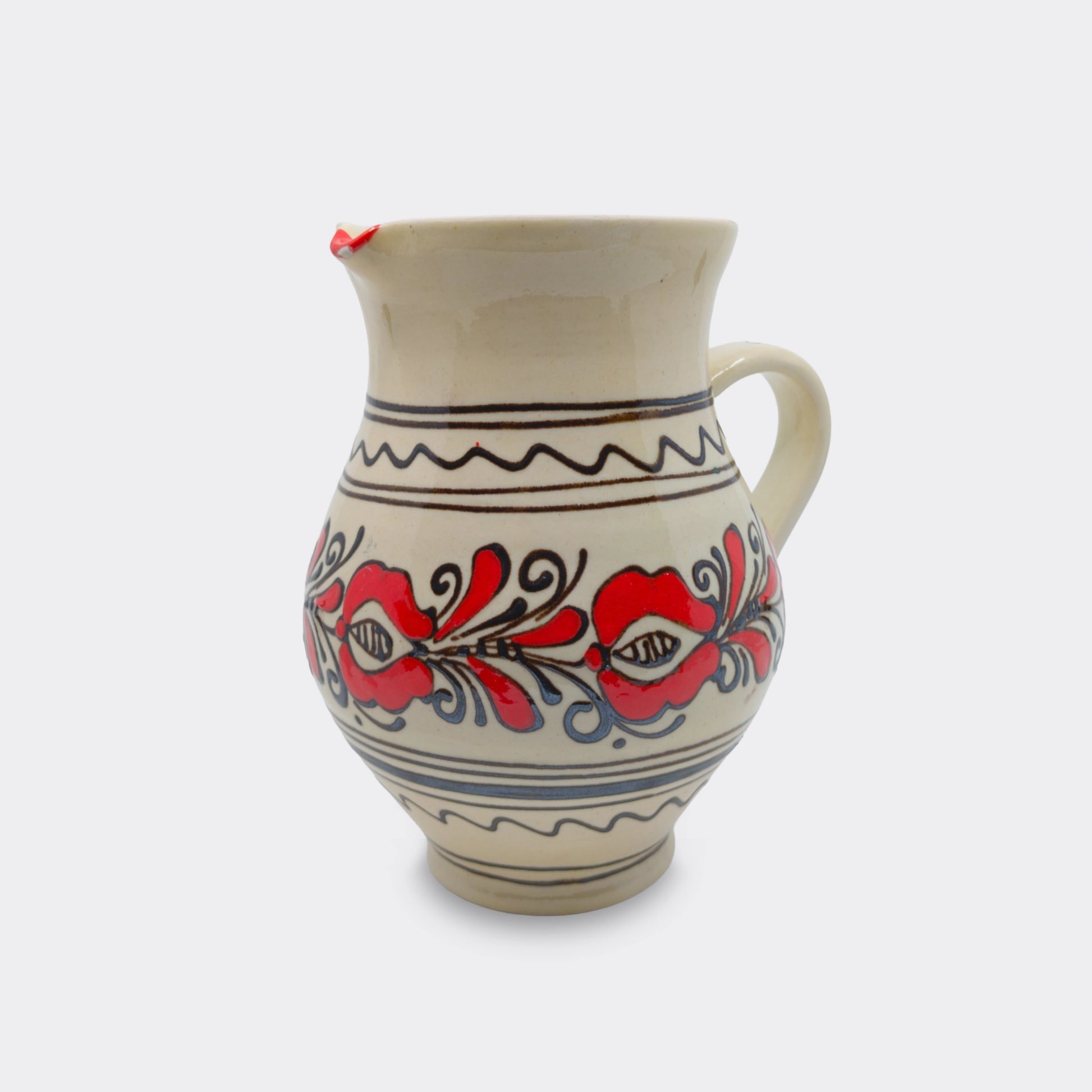 Pichet artisanal en faïence de Corund peint à la main. Décor floral rouge sur émail crème avec frises.