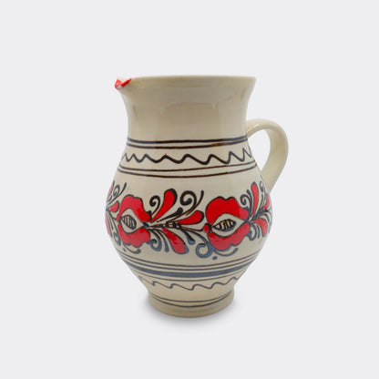 Pichet artisanal en faïence de Corund peint à la main. Décor floral rouge sur émail crème avec frises.