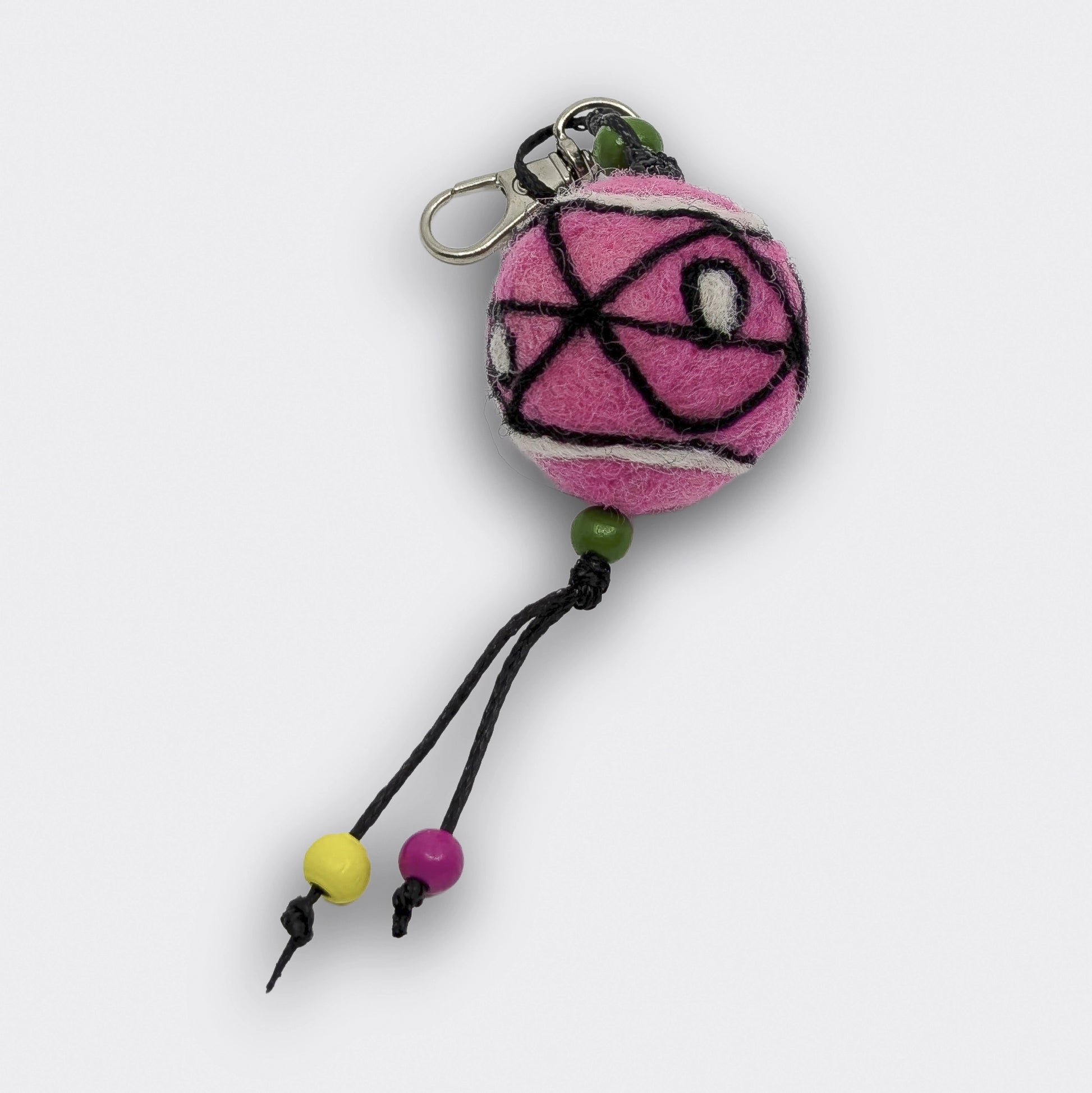 Breloque de sac constituée d'une boule de feutre rose avec des lignes géométriques noires. Attache mousqueton.