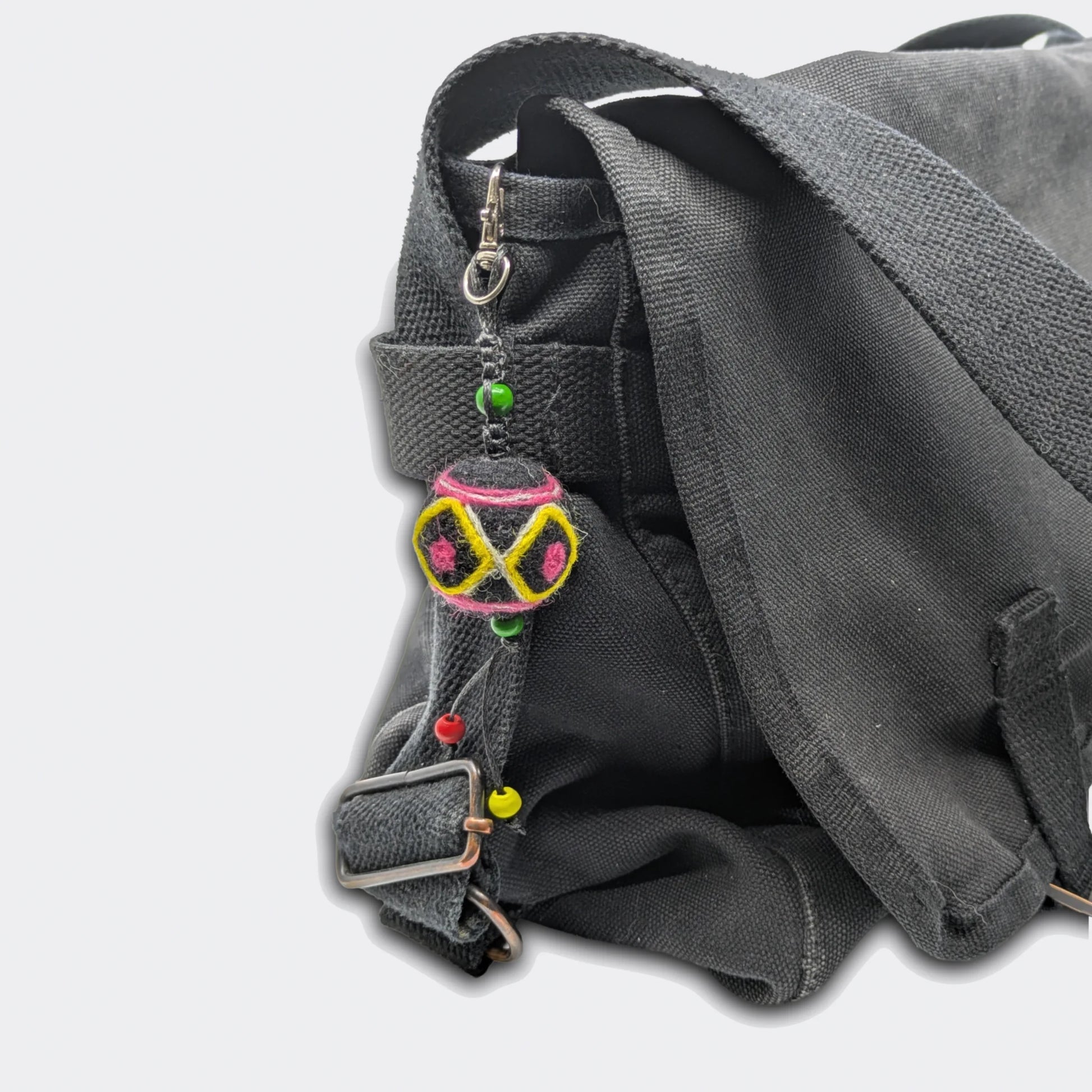 Porte-clé artisanal Voïvod, décoration géométrique jaune et rose sur feutre noir. Vue sur sac
