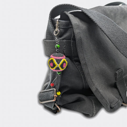 Porte-clé artisanal Voïvod, décoration géométrique jaune et rose sur feutre noir. Vue sur sac