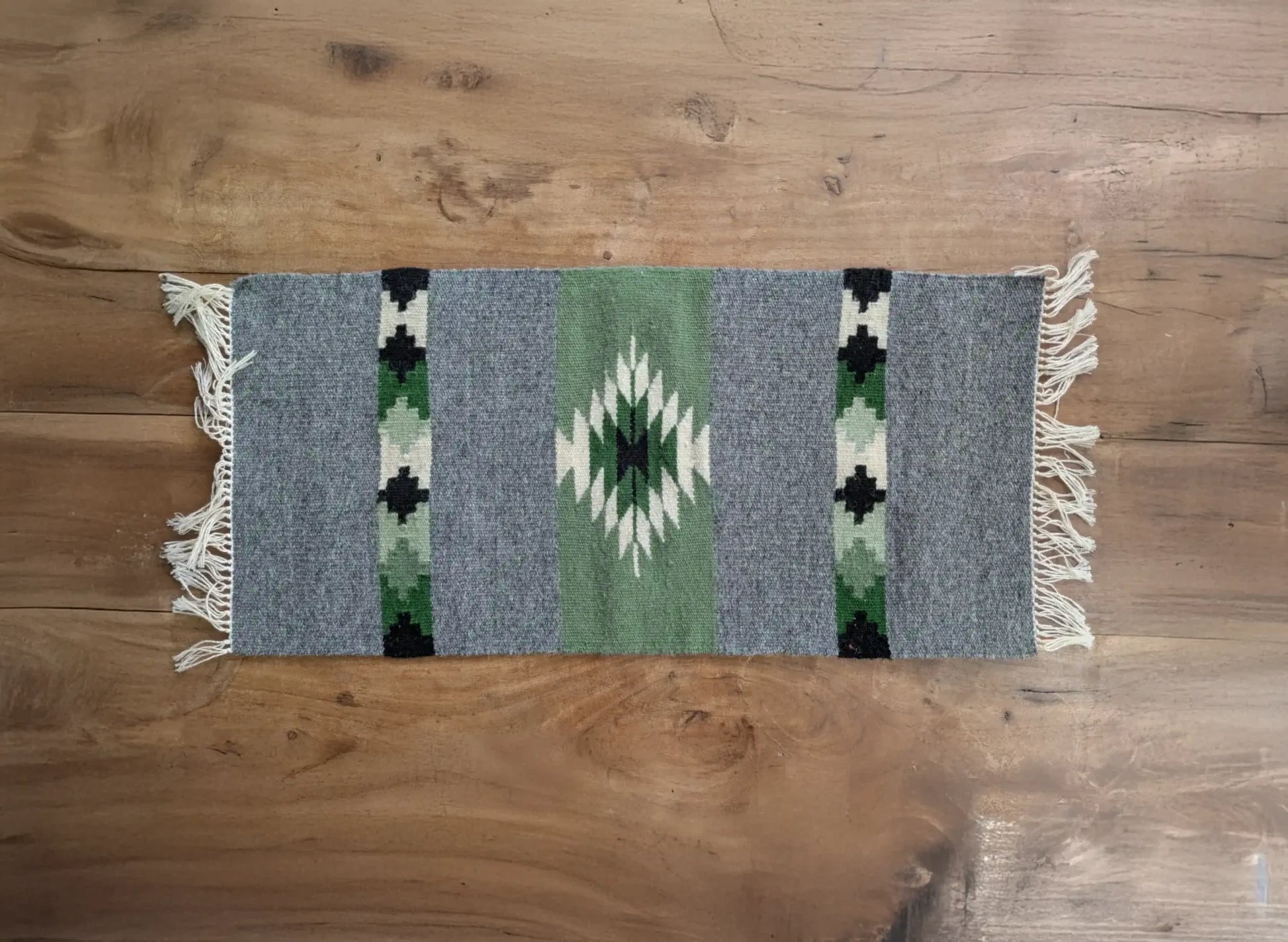 Petit tapis en laine gris et vert sauge tissé à la main. Un motif losange inspiré des textiles balkaniques structure la surface. Tapis artisanal au style géométrique.