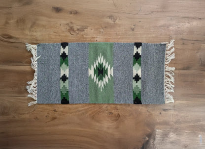 Petit tapis en laine gris et vert sauge tissé à la main. Un motif losange inspiré des textiles balkaniques structure la surface. Tapis artisanal au style géométrique.