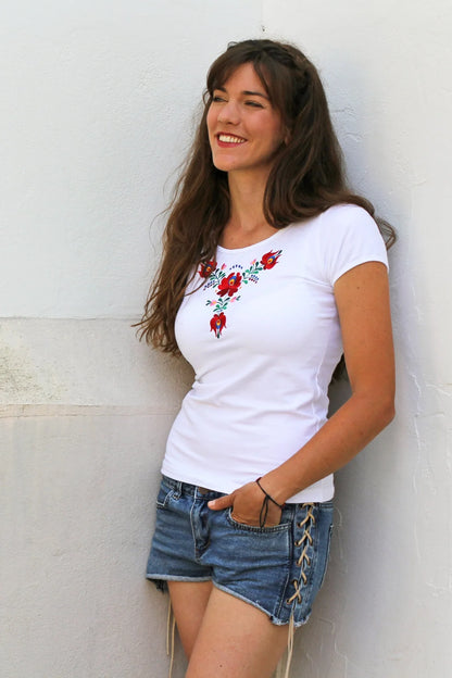 T-shirt blanc à manches courtes agrémenté de broderies traditionnelles Matyó en Hongrie. La broderie estsituée sous le col rond. Photo légèrement en biais.