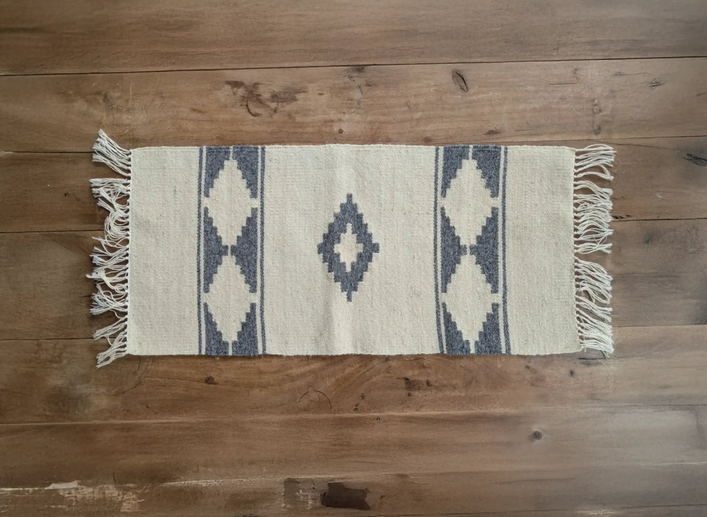 Petit tapis en laine crème et bleu tissé main. Les losanges géométriques rappellent les tissages balkaniques. Un tapis artisanal sobre et clair.