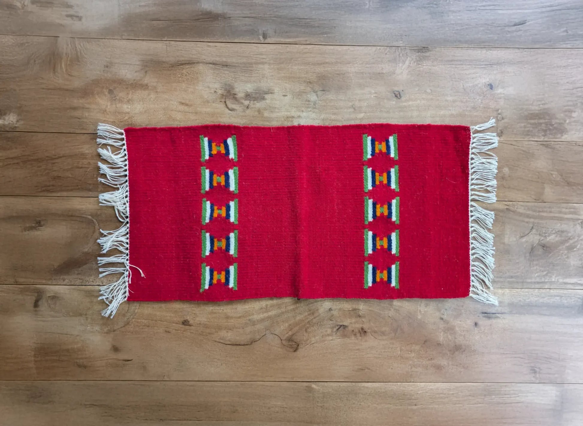 Tapis artisanal rouge avec un motif central et deux lignes colorées inspirées. Format idéal pour une petite zone de passage.