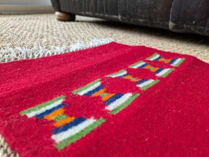 Détail d'un petit tapis rouge en laine, montrant des petites figures multicolores. Le tissage est serré et légèrement granuleux. Tissé à la main au Monténégro.