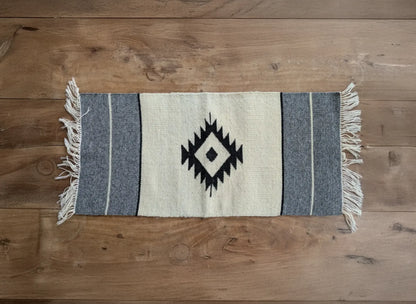 Tapis balkanique en laine tissé main, blanc cassé et gris. Le motif central en losange apporte une touche traditionnelle. Une pièce sobre aux lignes simples.