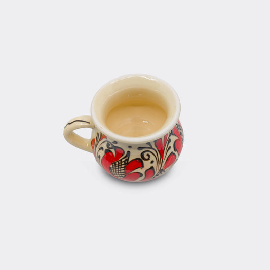 Tasse artisanale roumaine en faïence de Corund, motif rouge et contours brun-noir sur glaçure crème intérieure et extérieure. Vue du dessus.