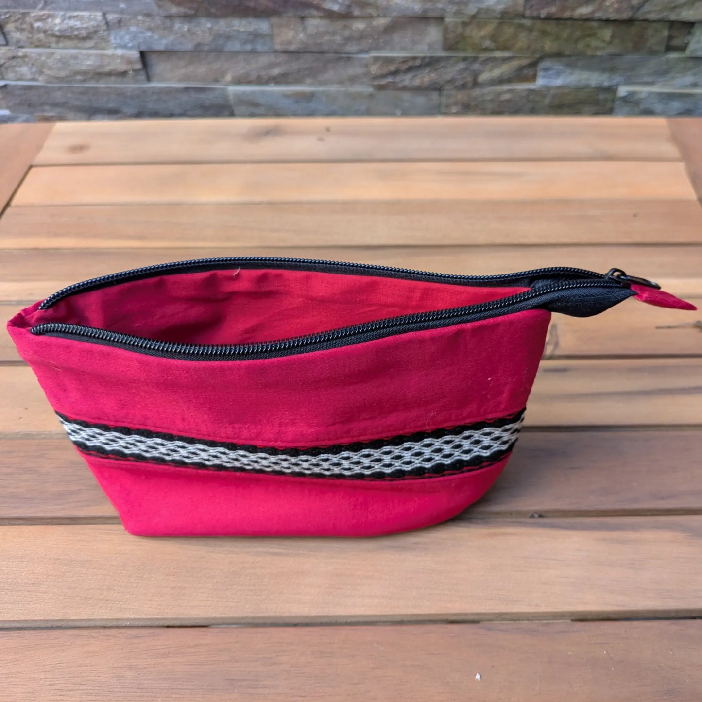 Trousse rouge zippée vue ouverte, avec doublure rouge et bande tissée décorative sur la face extérieure.