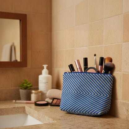 Trousse de toilette tissée main au métier, coton bleu et blanc, posée sur un plan de salle de bain avec miroir et flacons.