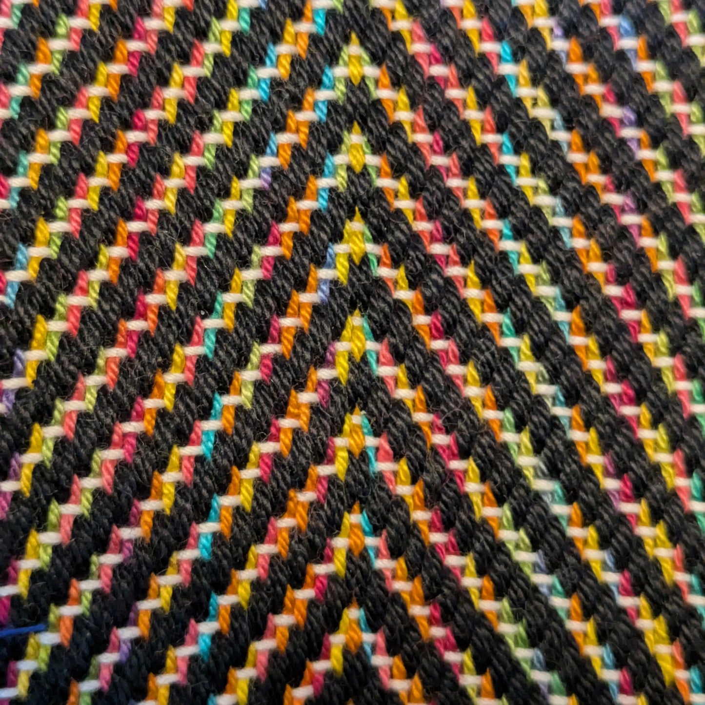 Détail du tissage manuel au métier, structure colorée et relief doux, trame noire accentuant la luminosité des fils.