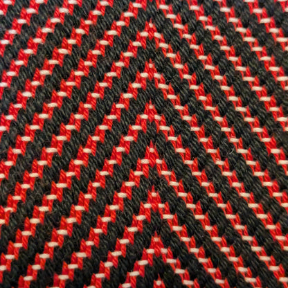 Gros plan du tissage sergé à chevrons, fils noirs épais et fils rouges fins, relief textile doux et régulier, fabrication artisanale.
