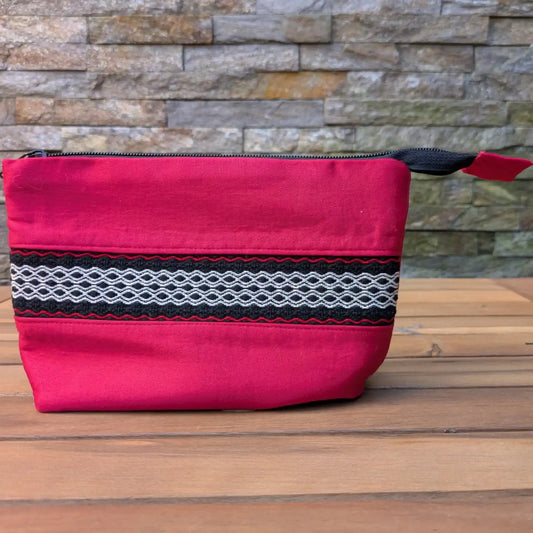 Trousse de toilette artisanale rouge avec bande tissée décorative noire, blanche et rouge sur le devant.
