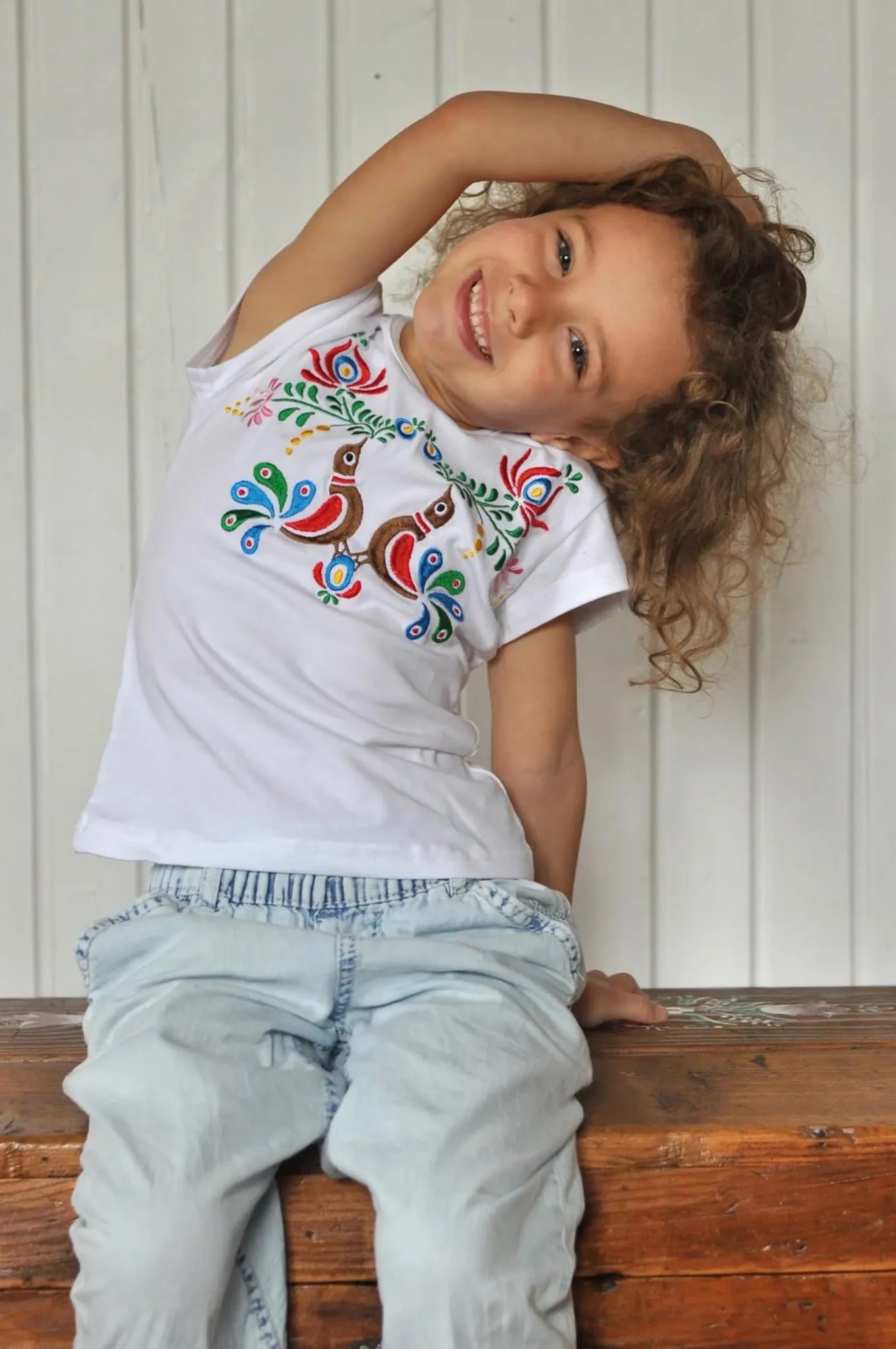 T-shirt blanc à manches courtes et à col rond agrémenté d'une magnifique broderie traditionnelle hongroise de type Matyó. Avec fleurs et oiseaux. Vue d'ensemble, un peu plus éloignée.
