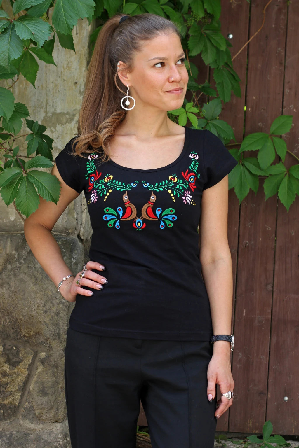 T-shirt noir à manches courtes avec une broderie caractéristique du style hongrois Matyó. Deux oiseaux colorés au centre et des fleurs aux mêmes tons ressortent magnifiquement sur le noir de ce haut.