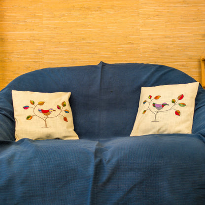 Housses de coussin ornées d'une broderie représentant un oiseau coloré sur des fines branches.