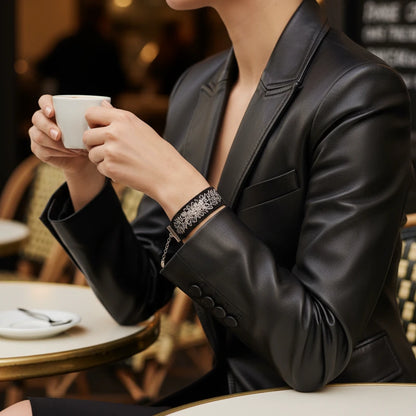 Bracelet artisanal noir, décoré de broderie argentée, présenté porté. Le fil capte la lumière avec finesse.