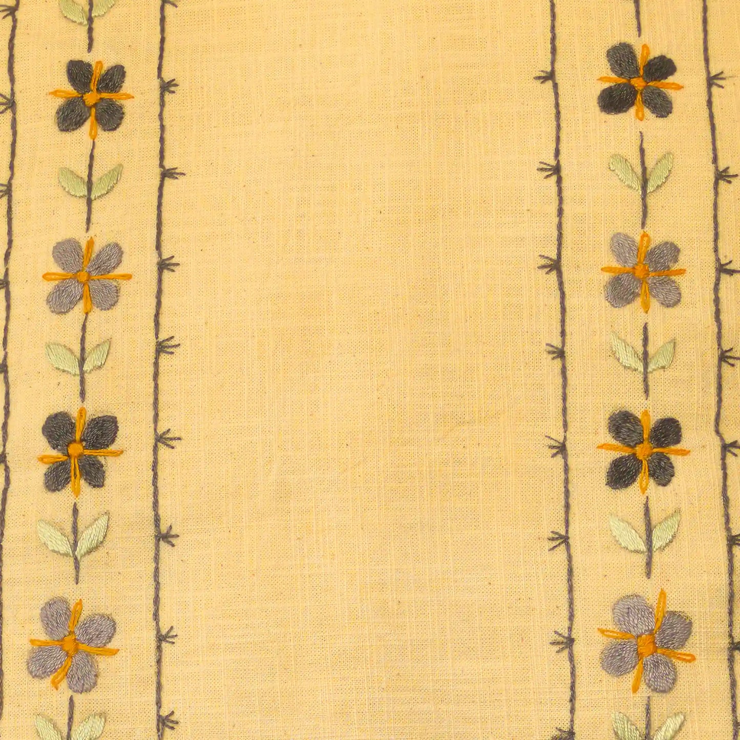 Gros plan sur une broderie en lin aux fleurettes répétées. Les motifs sont alignés verticalement. Un travail artisanal brodé main.