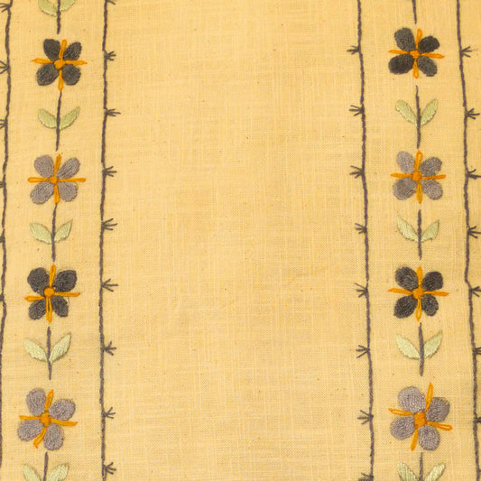 Gros plan sur une broderie en lin aux fleurettes répétées. Les motifs sont alignés verticalement. Un travail artisanal brodé main.