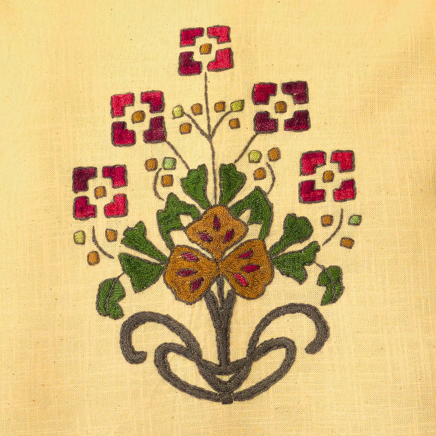 Gros plan sur le bouquet brodé main avec fleurs rouges carrées et fleur ocre centrale. Les bourgeons ponctuent les tiges. Un détail floral folk