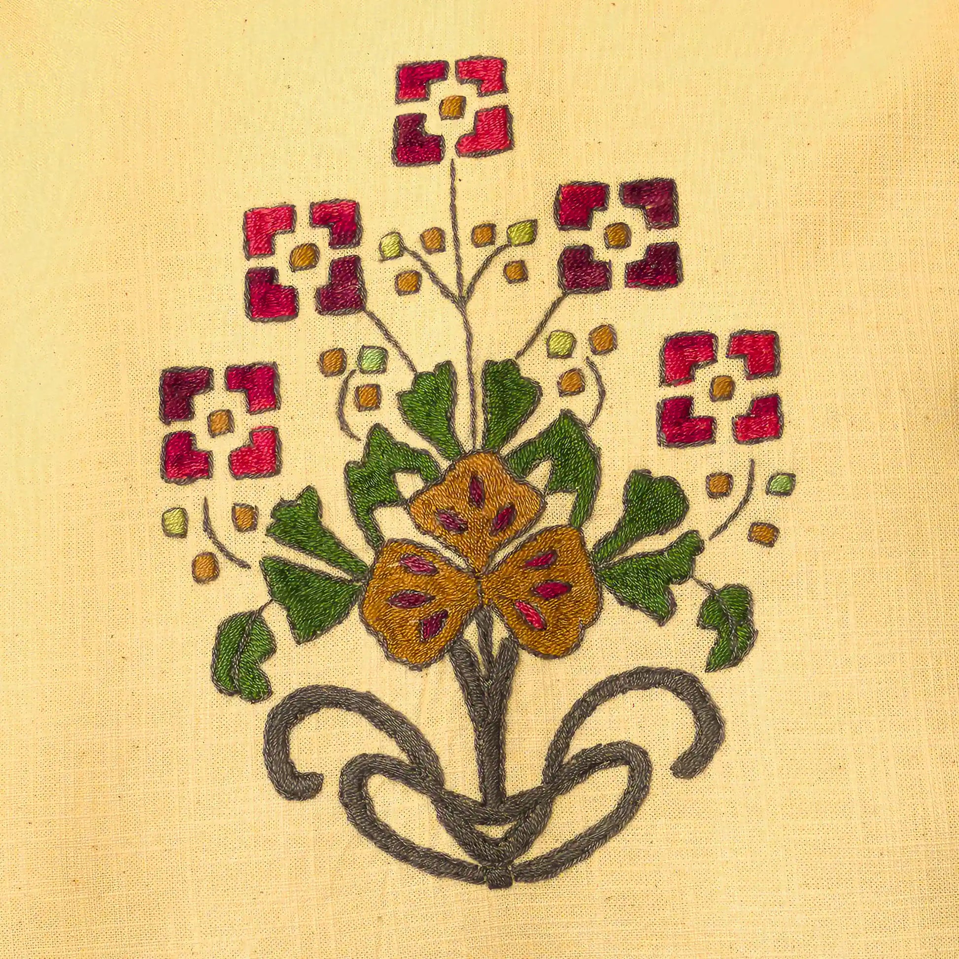 Gros plan sur le bouquet brodé main avec fleurs rouges carrées et fleur ocre centrale. Les bourgeons ponctuent les tiges. Un détail floral folk