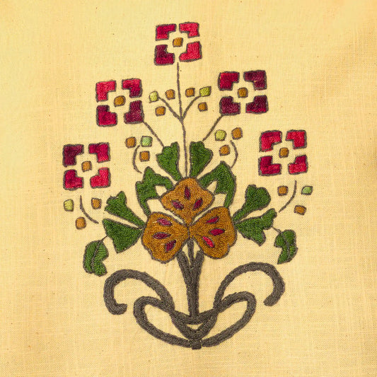 Gros plan sur le bouquet brodé main avec fleurs rouges carrées et fleur ocre centrale. Les bourgeons ponctuent les tiges. Un détail floral folk